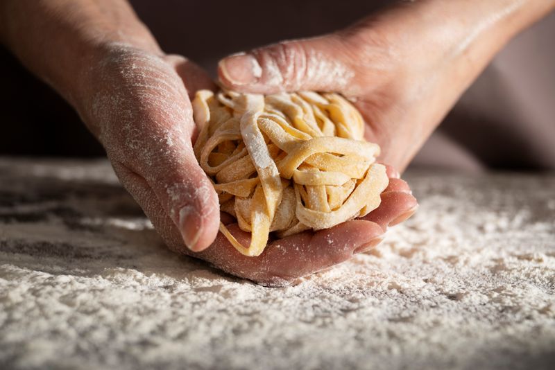 Hands holding a bundle of raw, fresh fettuccine noodles, dusted with flour.
