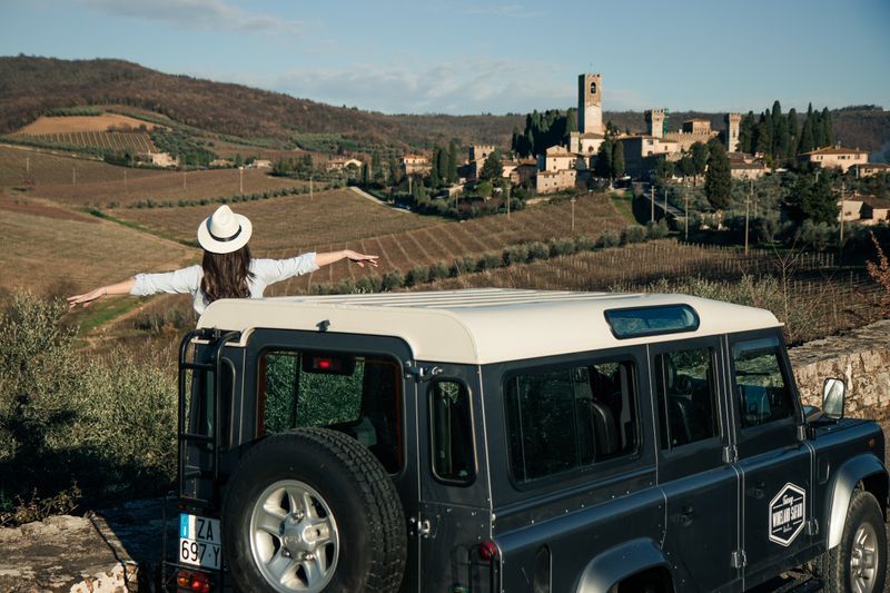A moment during a wineland safari tour in the Chianti hillside, where a woman whatches a medieval town from a Land Rover Defender.