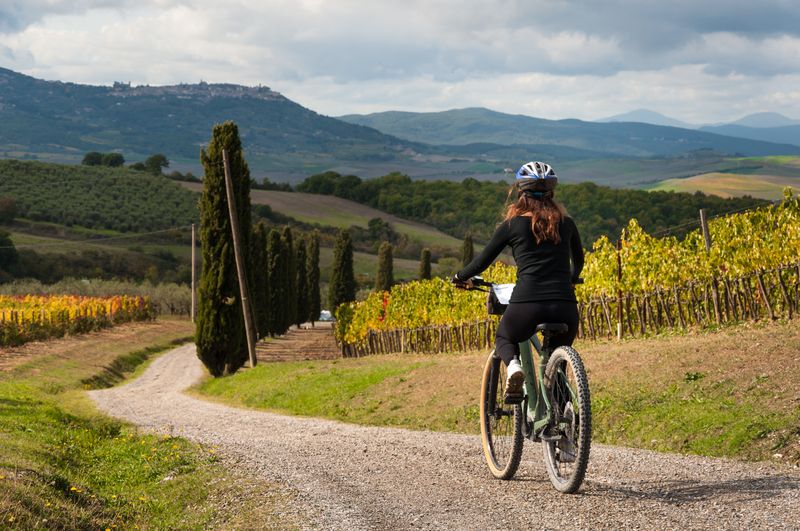 A woman on a cross-country bike, riding on a country road on tuscanian hills.
