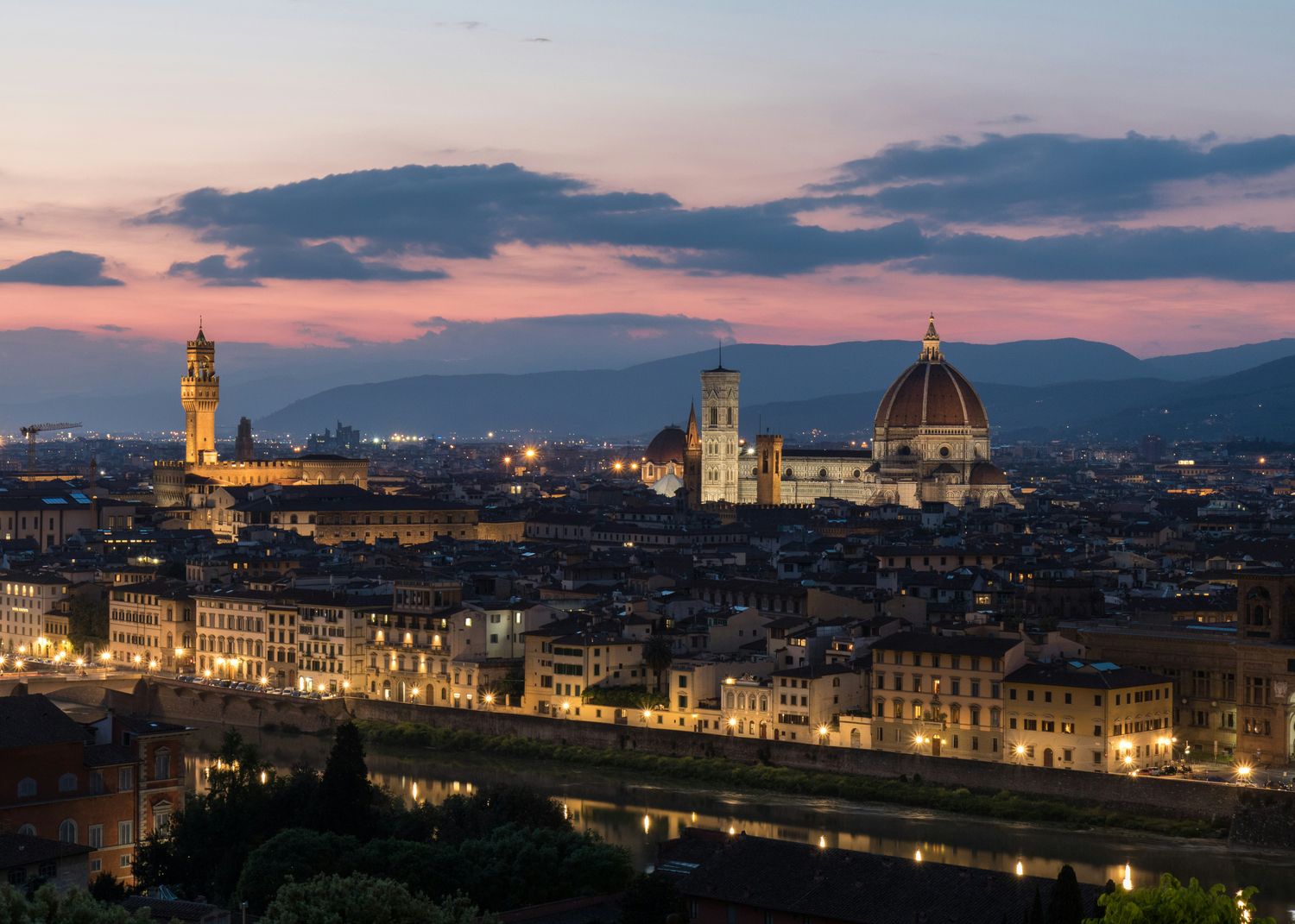 Panoramic view of Florence city center by night, encircled by the Apennines. The Basilica of Santa Maria Novella and Palazzo Vecchio are illuminated by artificial lights and tower above all the others medieval buildings.